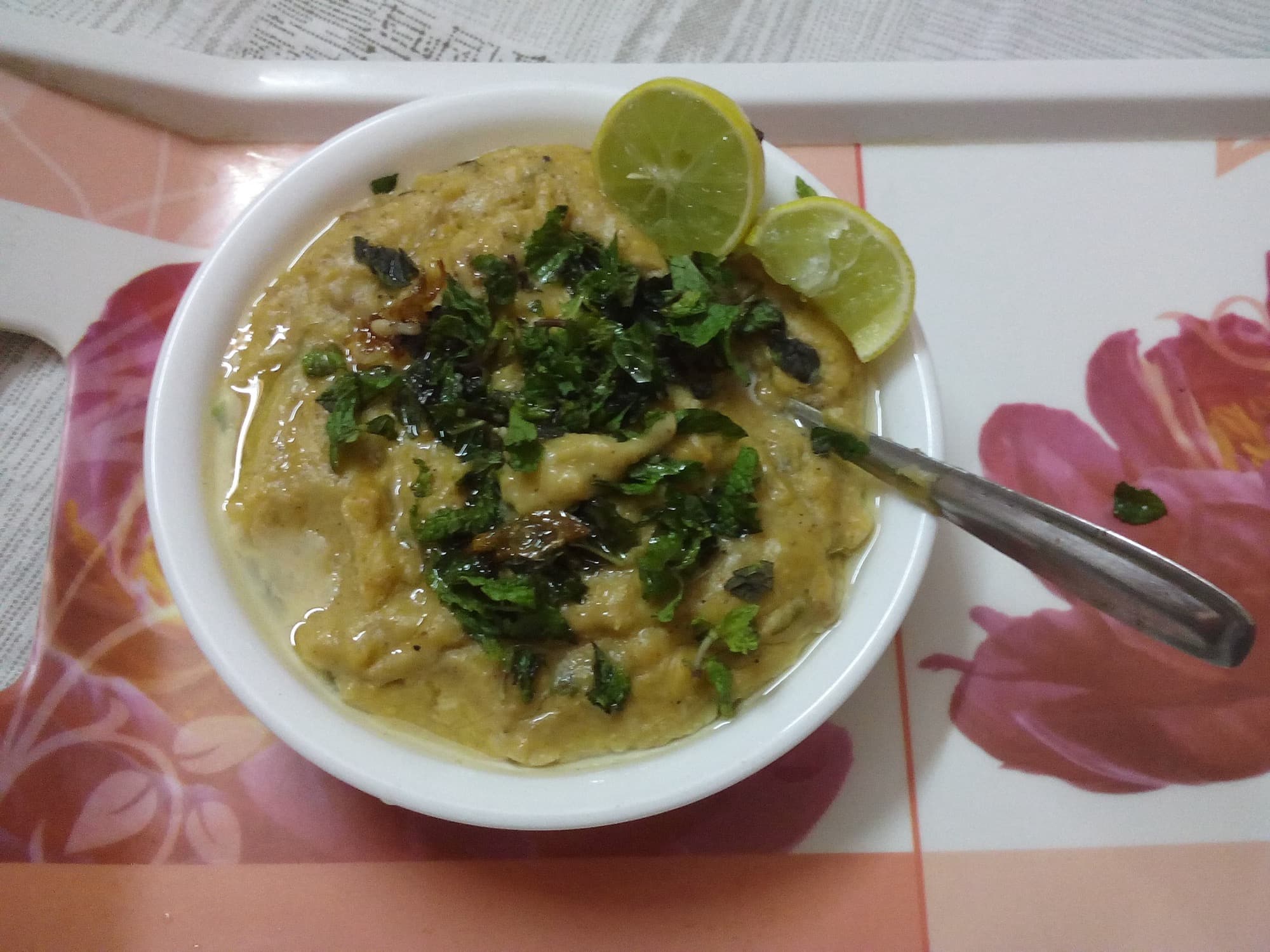 A bowl of Hyderabadi haleem topped with mint, fried onion, and lemon wedges