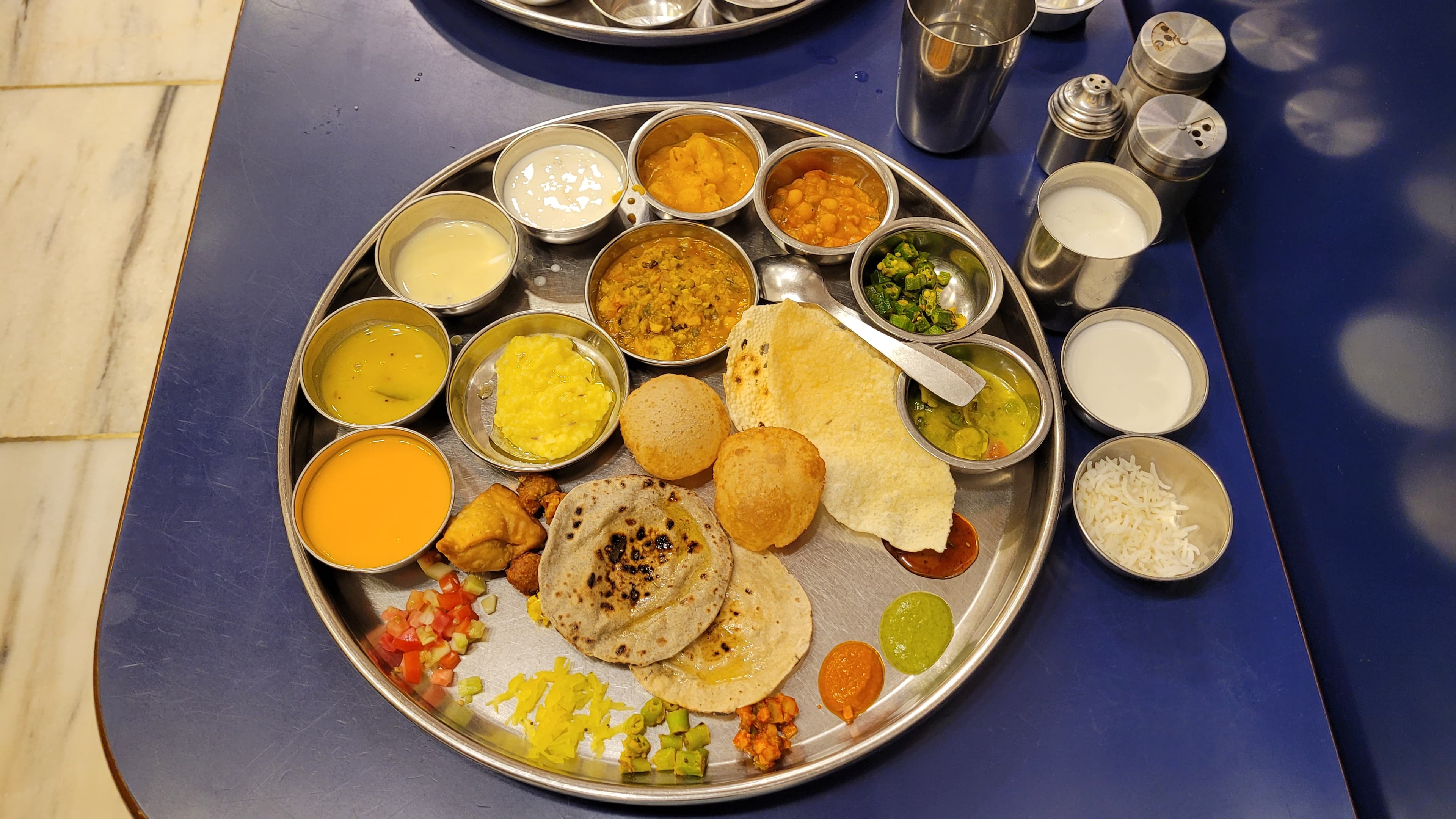 Gujarati thali with rotli, dal, kadhi, shaak, rice, farsan, chutneys, and sweets
