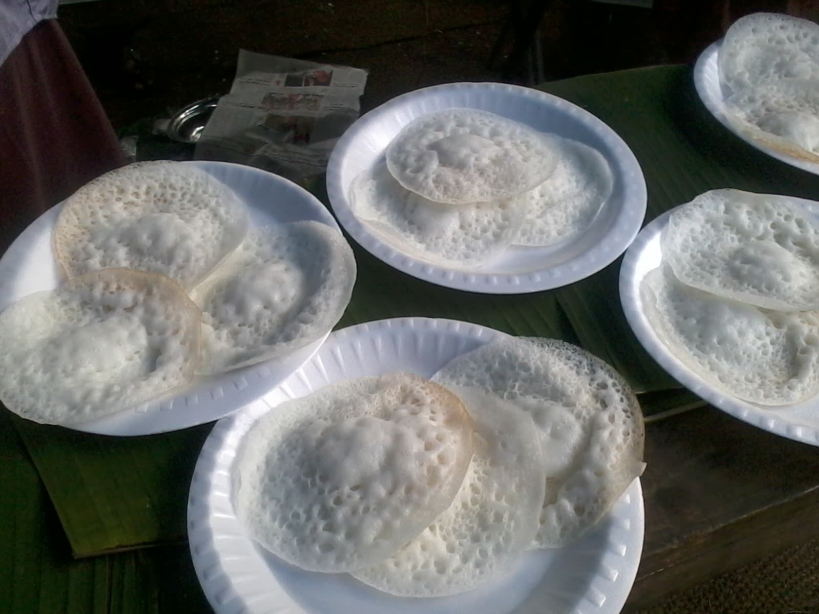 Stacks of lacy white appam on plates set over banana leaves
